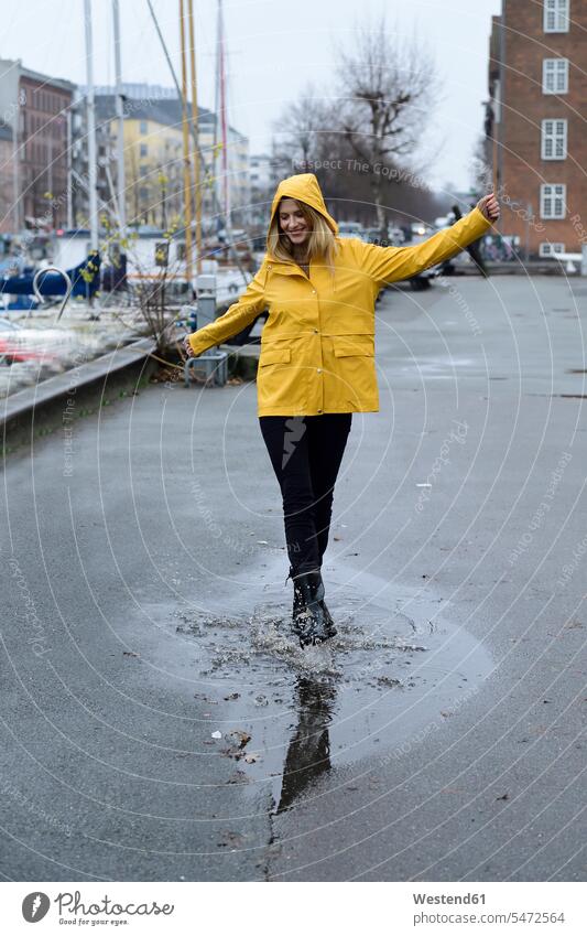 Denmark, Copenhagen, happy woman jumping in puddles at city harbour town cities towns females women happiness pool Leaping outdoors outdoor shots location shot