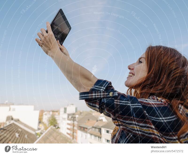 Smiling redheaded woman with tablet on rooftop terrace taking a selfie human human being human beings humans person persons caucasian appearance