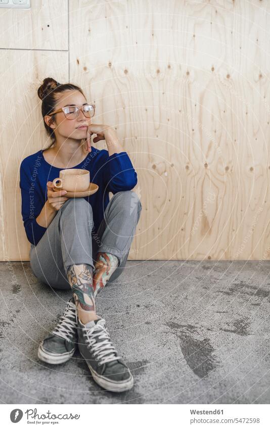 Young woman taking a break in office, drinking coffee from a wooden cup Coffee sitting on ground Sitting On The Floor Sitting On Floor Taking a Break resting