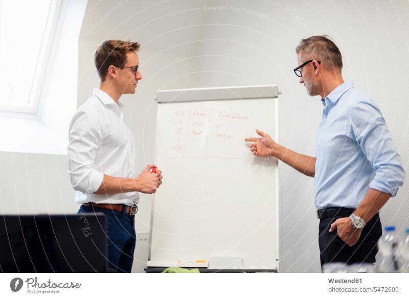 Two businessmen discussing at flip chart in office offices office room office rooms colleagues flipchart flip charts flipcharts discussion Businessman