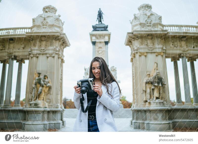 Smiling woman with a camera standing in front of Alfonso XII monument in El Retiro park, Madrid, Spain touristic tourists cameras photograph smile delight
