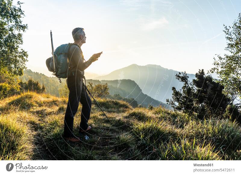 Man using mobile phone while standing on mountain against sky at sunrise, Orobie, Lecco, Italy color image colour image Orobie Mountains mountain range