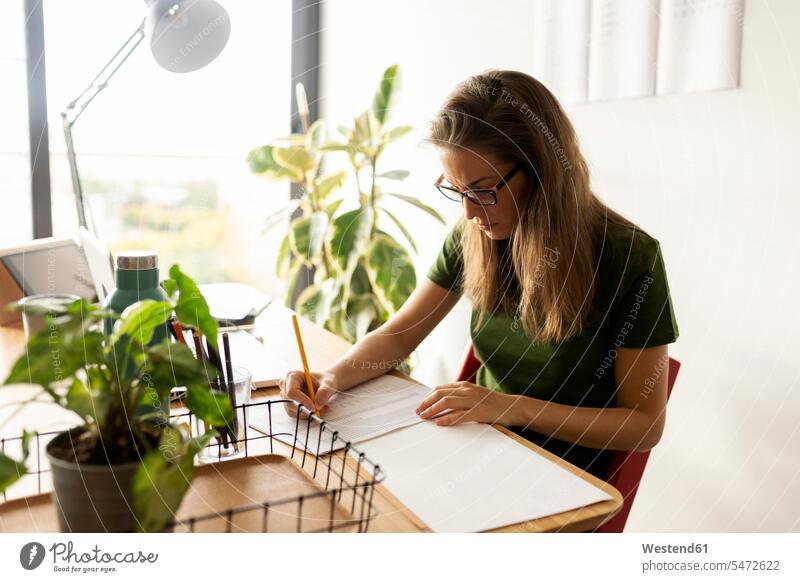 Businesswoman writing on paper while sitting in home office color image colour image Spain casual clothing casual wear leisure wear casual clothes Casual Attire