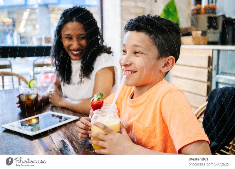 Cheerful woman looking at son sitting with fresh smoothie in restaurant color image colour image indoors indoor shot indoor shots interior interior view