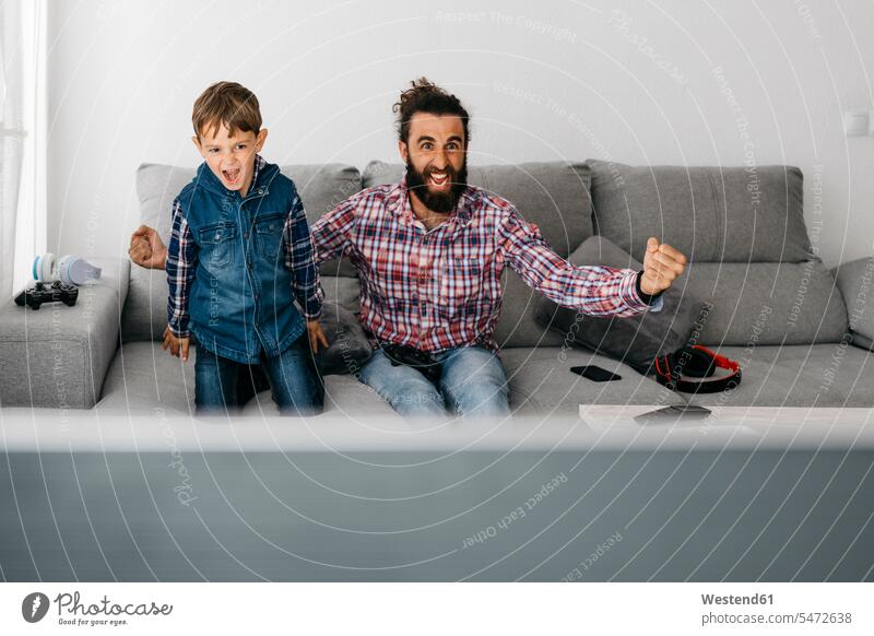 Portrait of father and son playing computer game together on the couch pa fathers daddy papa portrait portraits computer games sons manchild manchildren settee