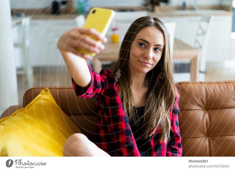 Young woman taking a selfie on a couch at home human human being human beings humans person persons celibate celibates singles solitary people solitary person