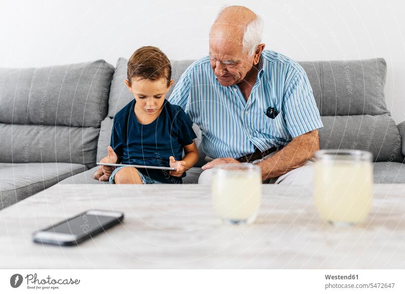 Grandfather and grandson sitting together on the couch at home looking at digital tablet digitizer Tablet Computer Tablet PC Tablet Computers iPad