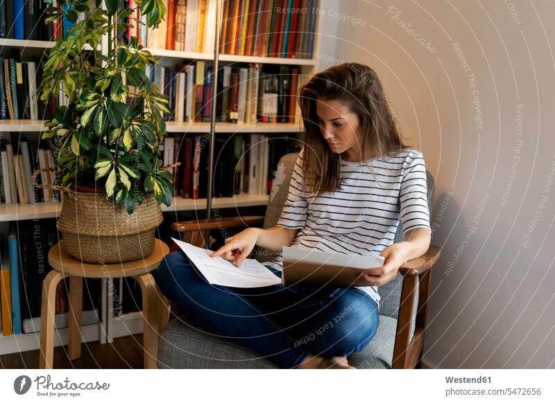 Businesswoman reading document while sitting on chair in home office color image colour image Spain casual clothing casual wear leisure wear casual clothes