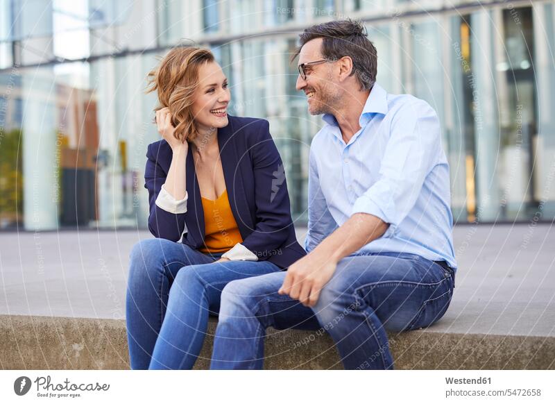 Two business people sitting outdoors talking businesspeople speaking Seated business world business life looking eyeing Fun having fun funny couple twosomes