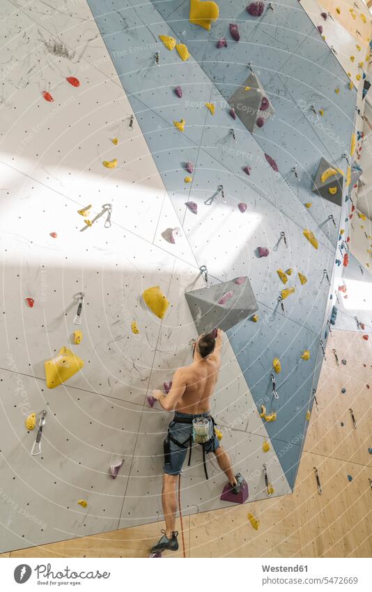 Shirtless man climbing on the wall in climbing gym (value=0) human human being human beings humans person persons short hairs short hairstyle short hairstyles
