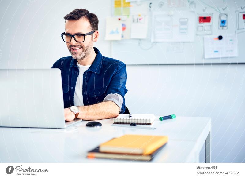 Casual businessman working on laptop at desk in office Businessman Business man Businessmen Business men offices office room office rooms desks casual At Work
