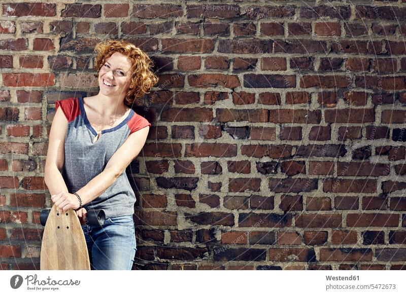 Smiling young woman with longboard standing at brick wall females women Longboard brick walls portrait portraits smiling smile Adults grown-ups grownups adult