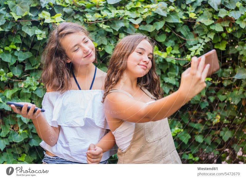 Young girls taking a selfie on ivy background friends mate female friend Hedgerow hedges relax relaxing photograph smile seasons summer time summertime summery