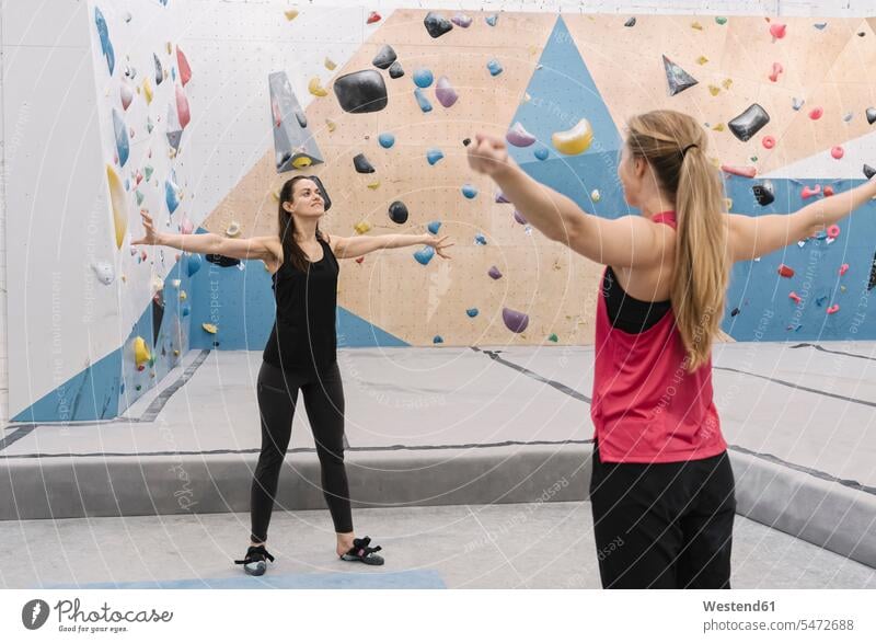 Two women doing stretching exercises before climbing on the wall (value=0) friends mate female friend practising train training exercising practice practise