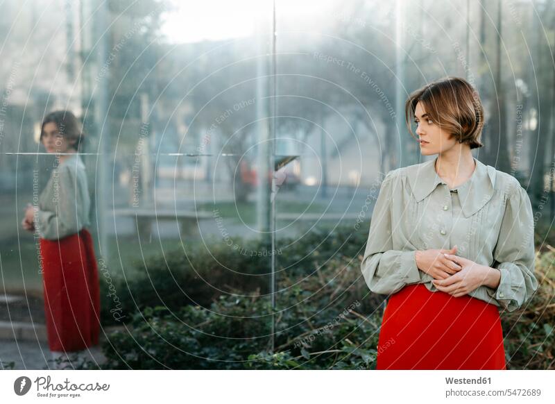 Portrait of woman with vintage clothes in an urban garden with reflection in the glass pane windows glass panes skirts Retro retro revival Retro Styled