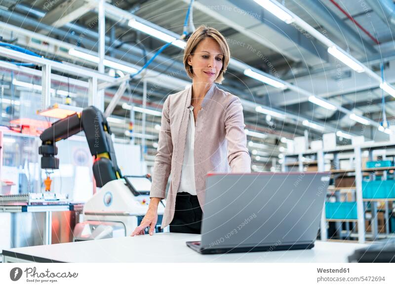 Businesswoman in a modern factory hall using laptop human human being human beings humans person persons caucasian appearance caucasian ethnicity european 1