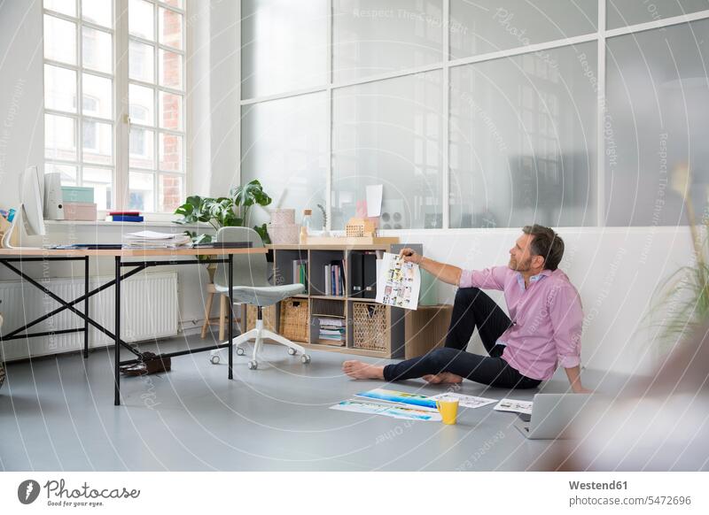 Casual man with plans and laptop sitting on the floor in a loft office offices office room office rooms Laptop Computers laptops notebook men males casual