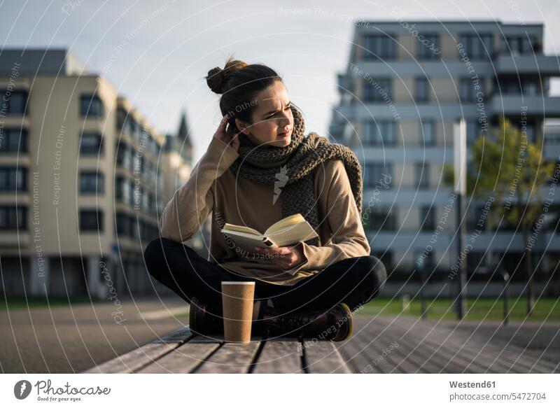Melancholy woman with coffee to go and book sitting on bench in autumn Coffee books females women Seated melancholy melancholic melancholia benches Drink