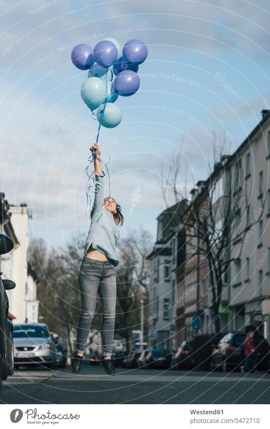 Young woman with blue balloons jumping in the air on the street road streets roads Leaping females women jump in the air decoration decorating decorations