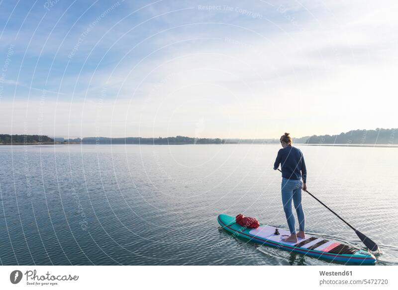 Woman standing on sup board in the morning on a lake seasons summer time summertime summery free time leisure time balanced Equilibrium on the go on the road