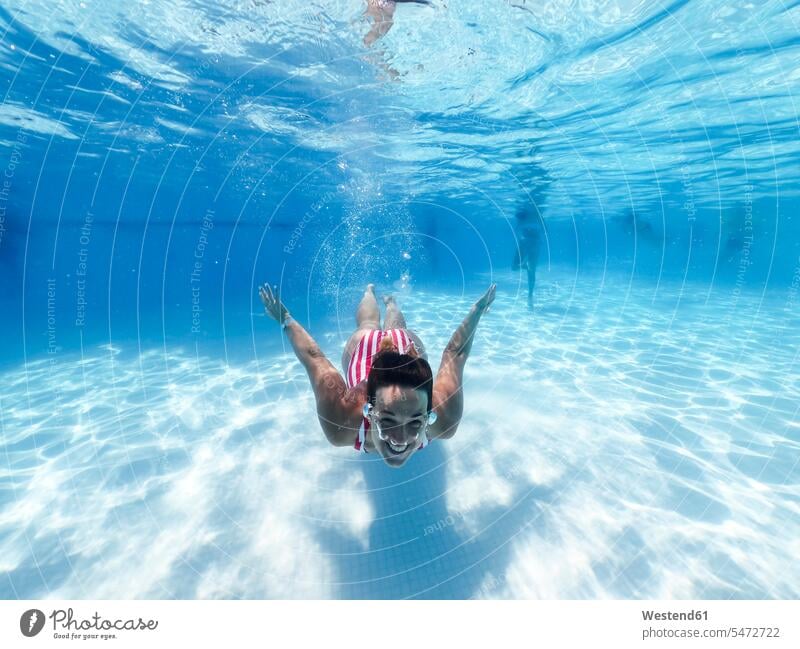 Smiling woman swimming underwater in pool at tourist resort color image colour image day daylight shot daylight shots day shots daytime leisure activity