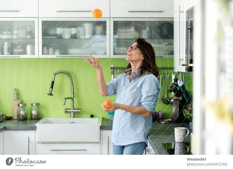 Mature woman juggling with oranges in kitchen at home Orange Oranges juggle females women domestic kitchen kitchens Fruit Fruits Food foods food and drink