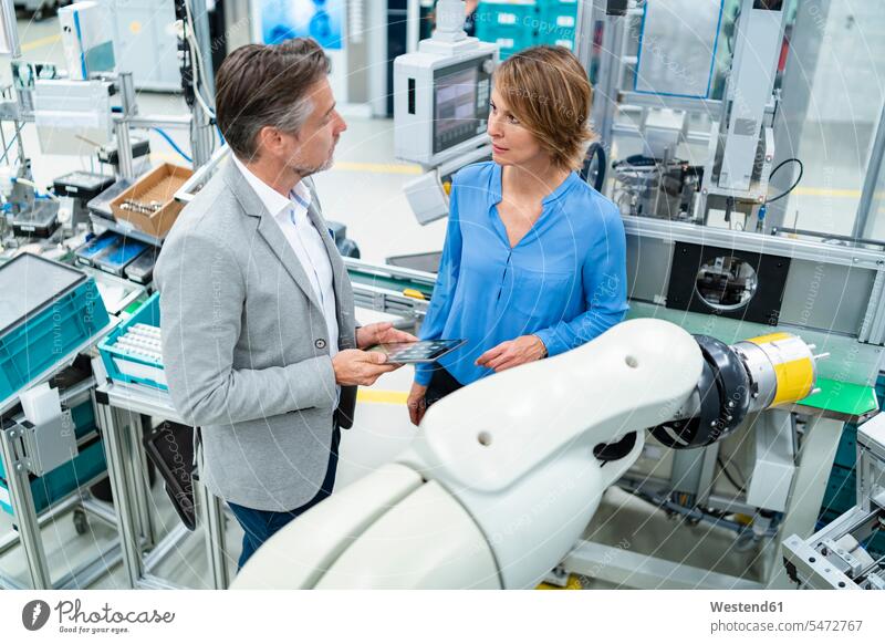 Businessman with tablet and woman talking at assembly robot in a factory human human being human beings humans person persons caucasian appearance
