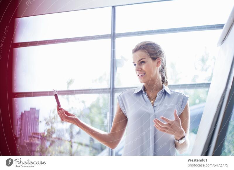 Confident young businesswoman explaining over flipchart during meeting in office color image colour image businesswomen business woman business women