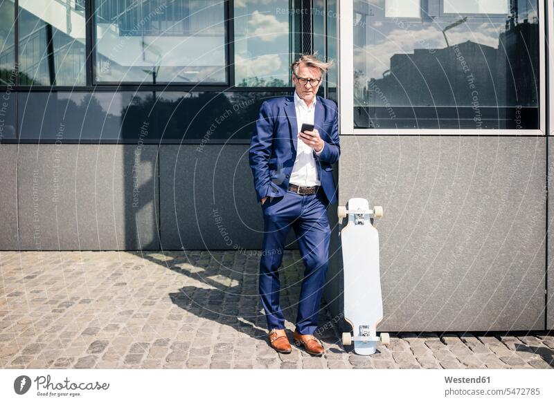 Mature businessman using cell phone outdoors next to longboard Longboard Businessman Business man Businessmen Business men mobile phone mobiles mobile phones