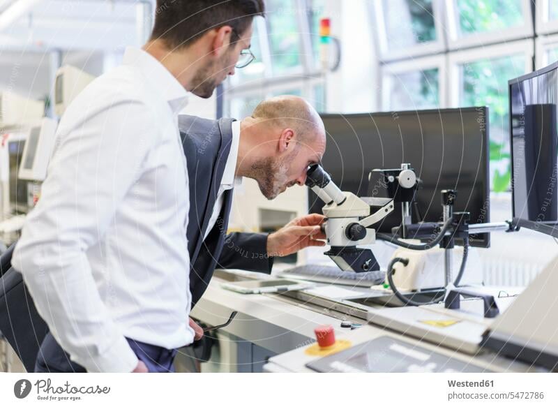 Young male technician standing by businessman looking through microscope at laboratory color image colour image indoors indoor shot indoor shots interior