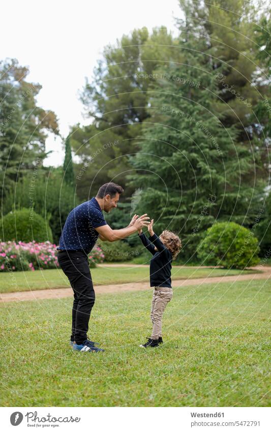 Father and son playing together in park parks father fathers daddy dads papa sons manchild manchildren parents family families people persons human being humans