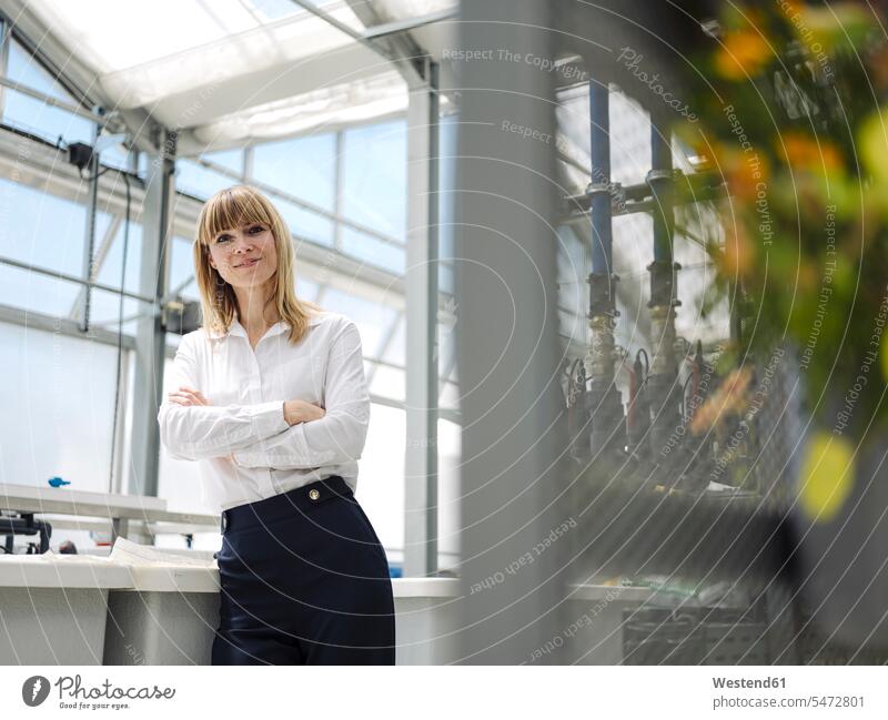 Confident businesswoman with arms crossed standing by window in greenhouse color image colour image Germany business people businesspeople Business Professional