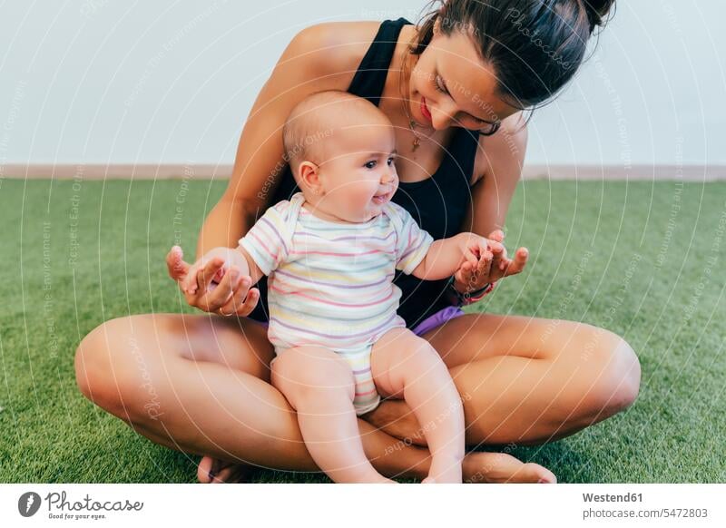 Young mother and baby exercising during mother child gymnastics carpets rug rugs exercise practising train training smile Seated sit delight enjoyment Pleasant