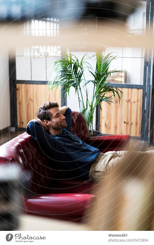Young man sitting on couch with closed eyes Seated men males settee sofa sofas couches settees Adults grown-ups grownups adult people persons human being humans
