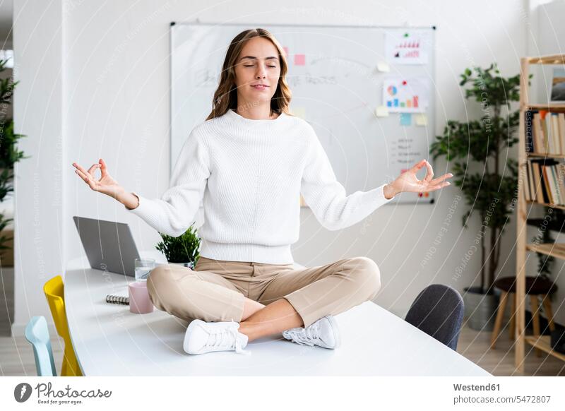 Young businesswoman practicing yoga while sitting on table at office color image colour image indoors indoor shot indoor shots interior interior view Interiors