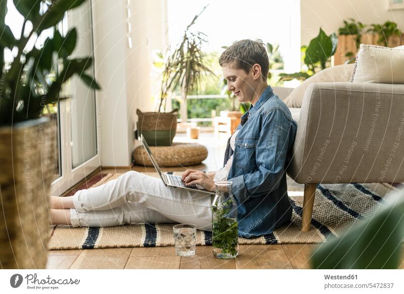 Mid adult woman with short hair using laptop while sitting on carpet at home color image colour image Germany leisure activity leisure activities free time