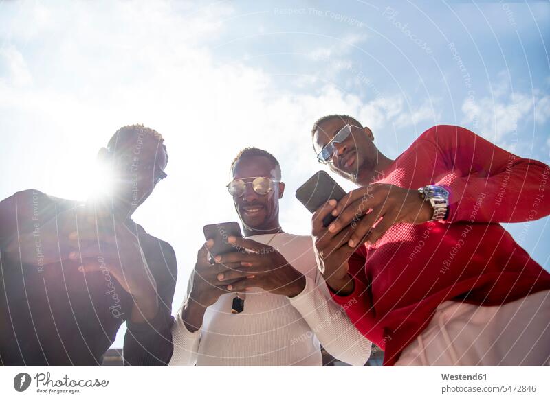 Three cool young men using cell phones in backlight human human being human beings humans person persons African black black ethnicity coloured Group