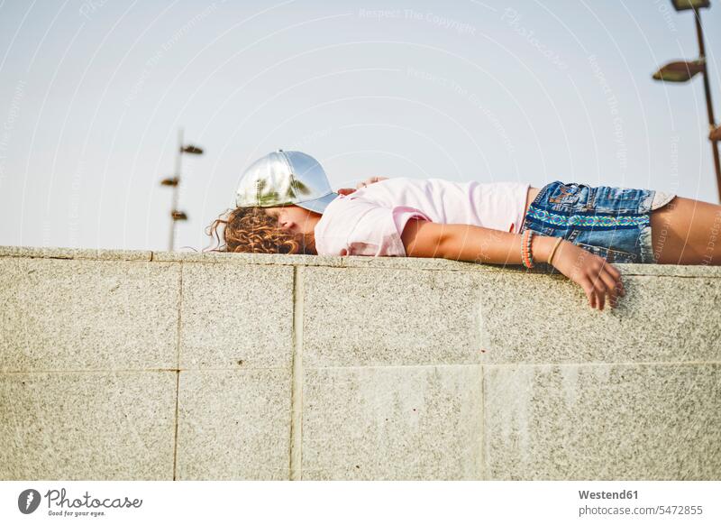 Girl lying on wall, basecap on head, obscured face Taking a Break resting break obscured faces face obscured face hidden leisure free time leisure time