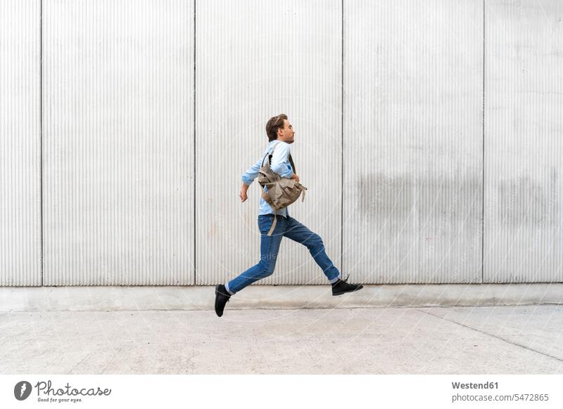 Casual businessman jumping in front of a wall business life business world business person businesspeople Business man Business men Businessmen back-pack