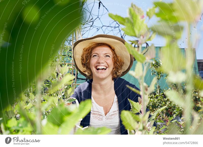 Portrait of happy young woman wearing straw in urban garden happiness females women straw hat straw hats portrait portraits Urban Gardening Urban Farming