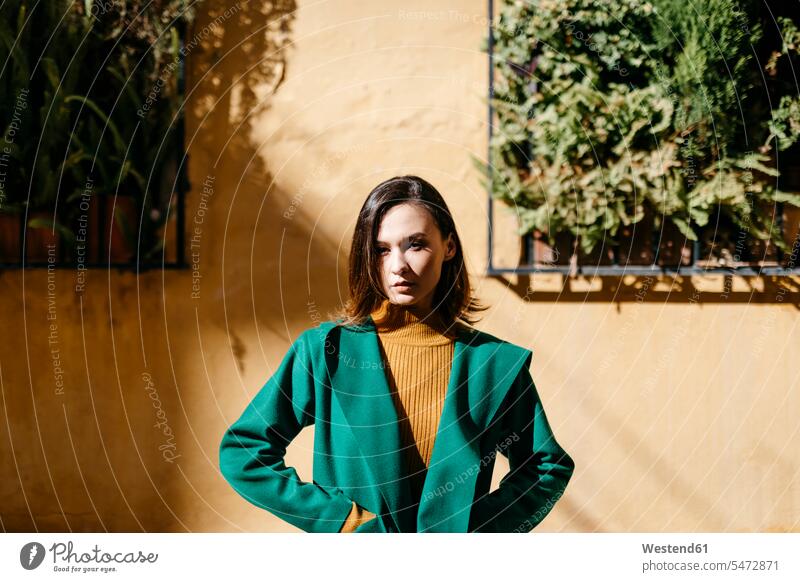 Beautiful woman wearing green jacket standing against building in city on sunny day color image colour image Spain casual clothing casual wear leisure wear