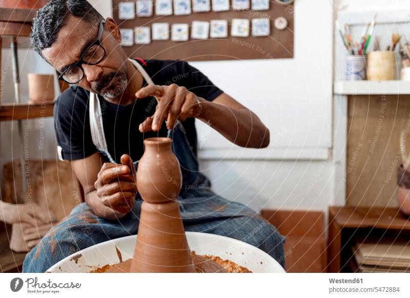 Close-up of male potter making earthenware while sitting in workshop color image colour image Spain indoors indoor shot indoor shots interior interior view