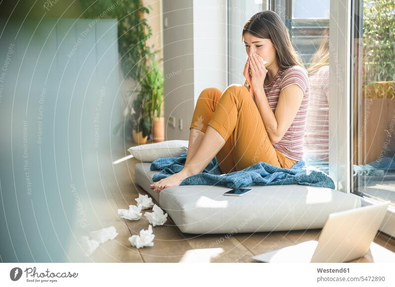 Young woman sitting at the window at home with laptop blowing her nose Laptop Computers laptops notebook blowing nose honking Seated tissue tissue handkerchief