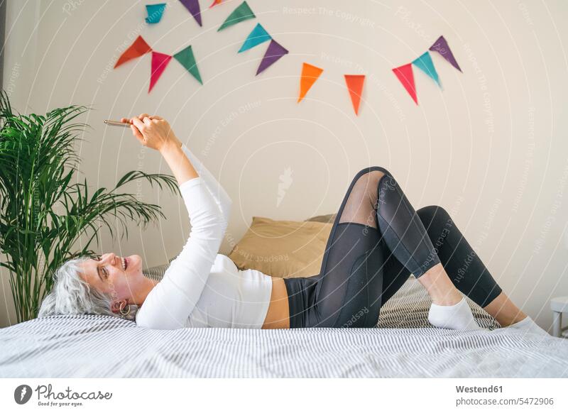 Happy woman lying on bed at home taking a selfie human human being human beings humans person persons celibate celibates singles solitary people solitary person