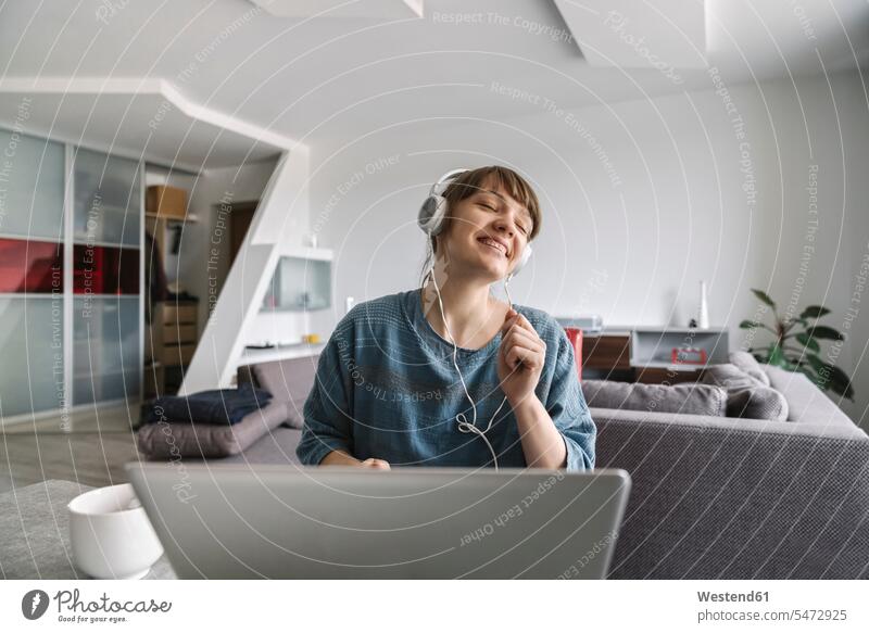 Happy woman wearing headphones and using laptop at home human human being human beings humans person persons celibate celibates singles solitary people