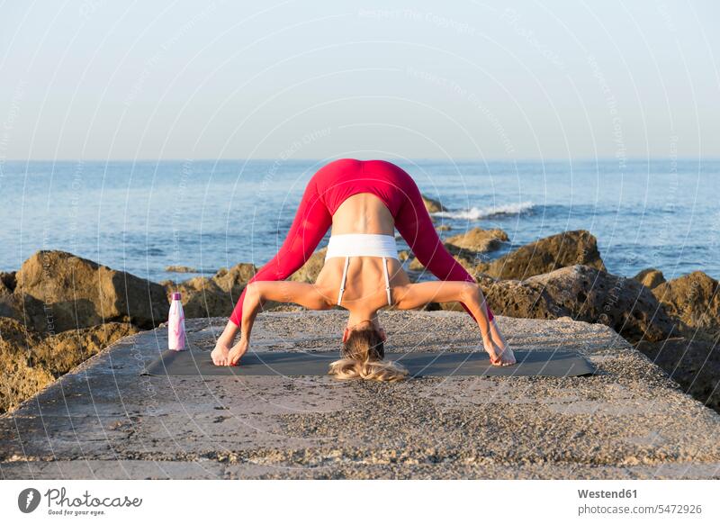 Young woman practicing yoga on the beach, doing prasarita padottanasana exercise exercising practice practise practising in the morning flexible Force Power