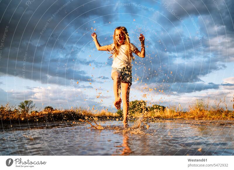 Cheerful girl splashing water on puddle against cloudy monsoon sky color image colour image Spain outdoors location shots outdoor shot outdoor shots day