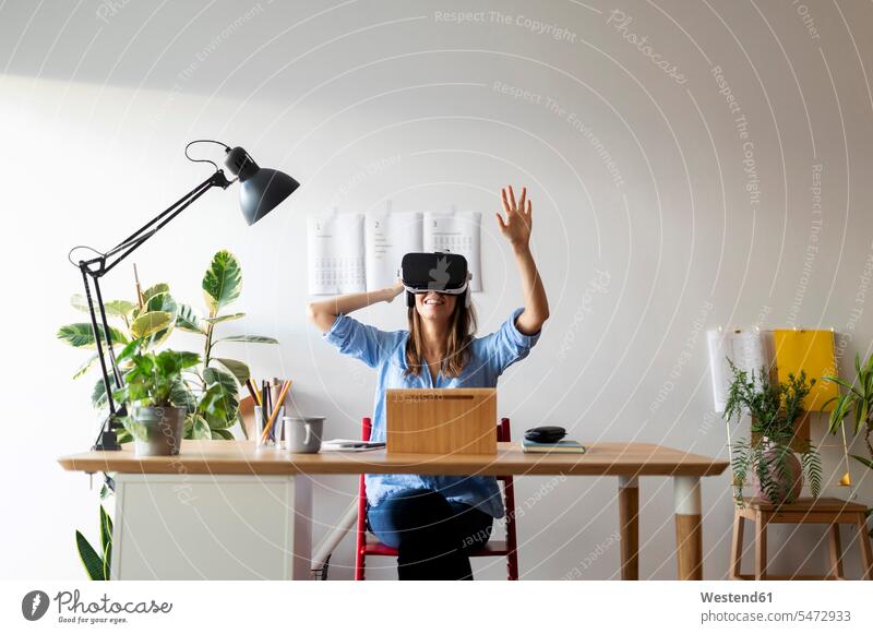 Young woman looking through virtual reality simulator while sitting at desk in home office color image colour image Spain casual clothing casual wear