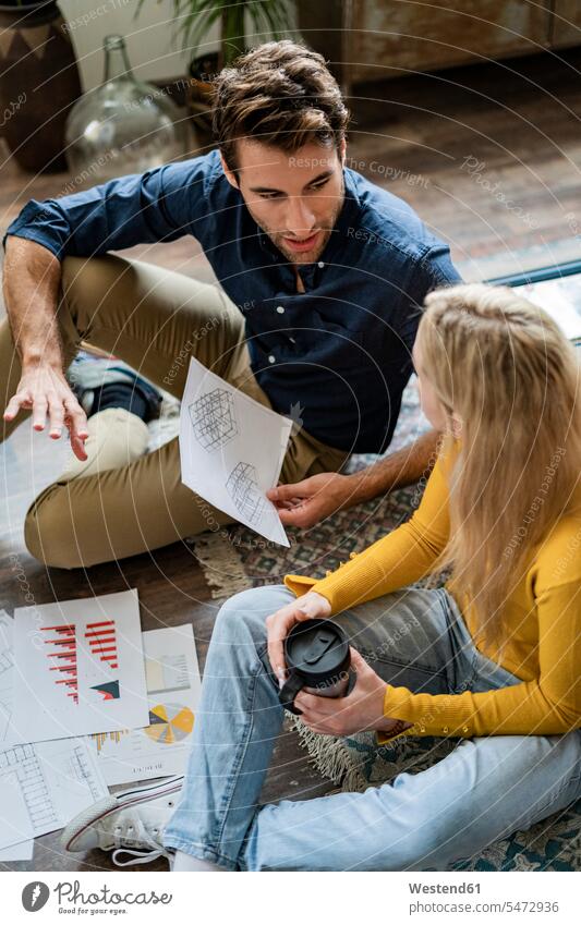Businessman and businesswoman sitting on the floor discussing documents in loft office discussion Business man Businessmen Business men floors Seated