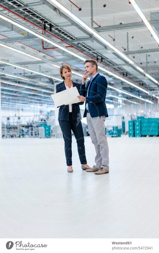 Businessman and businesswoman discussing plan in a factory hall business life business world business person businesspeople associate associates